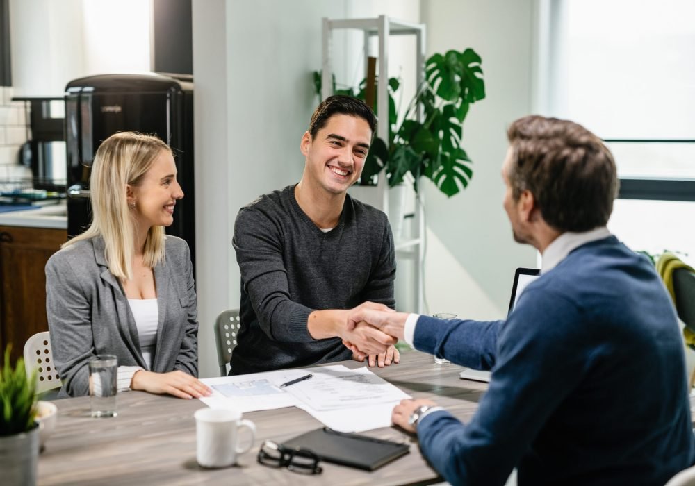 Happy couple shaking hands with their real estate agent at home.